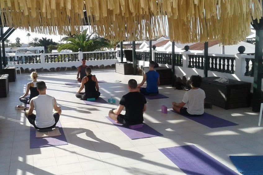 Des personnes sont assises sur des tapis de yoga dans un cadre extérieur, sous une pergola. 1