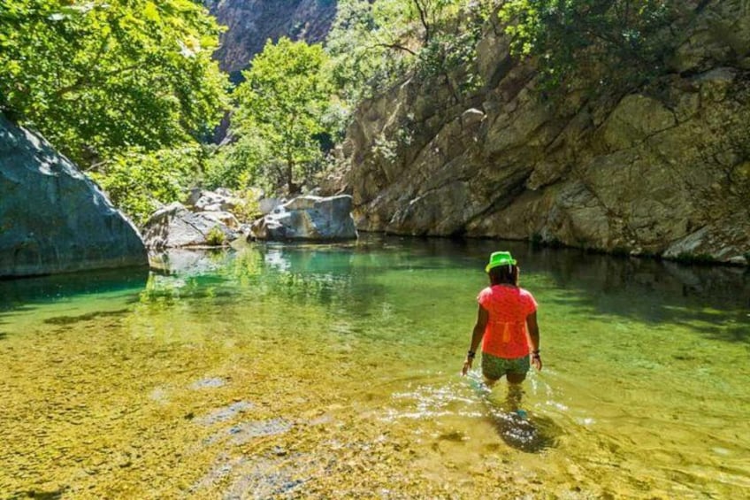A person wading in a clear river surrounded by rocky cliffs and greenery. 2