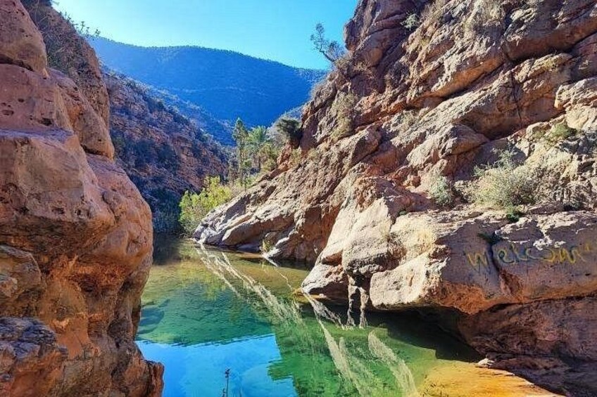 A canyon with a clear water stream, rocky cliffs, and a mountain in the background. 4