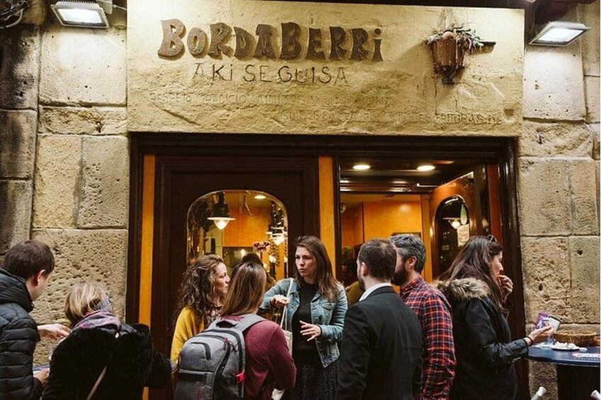 A group of people standing outside a restaurant named Bordaberri. 1