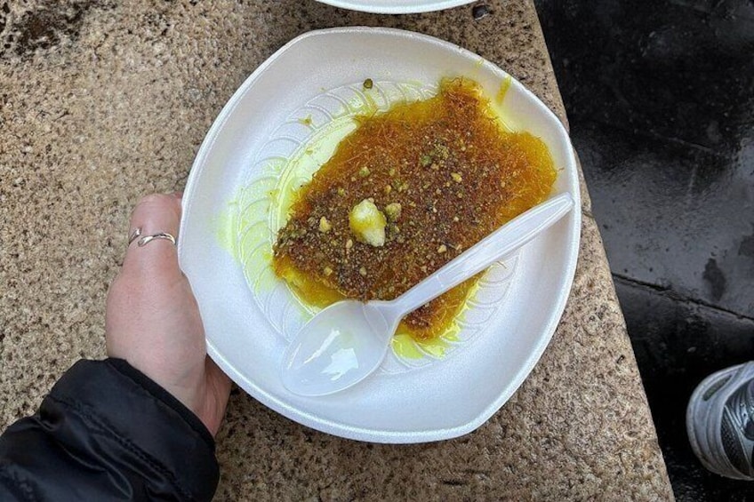 Une personne tient un bol blanc dans lequel se trouve une cuillère. Le bol contient un dessert brun, nappé d’une sauce jaune et agrémenté de quelques éléments verts. 2