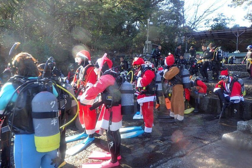 People in red and white costumes with scuba gear, standing on a wet surface with trees in the background. 4
