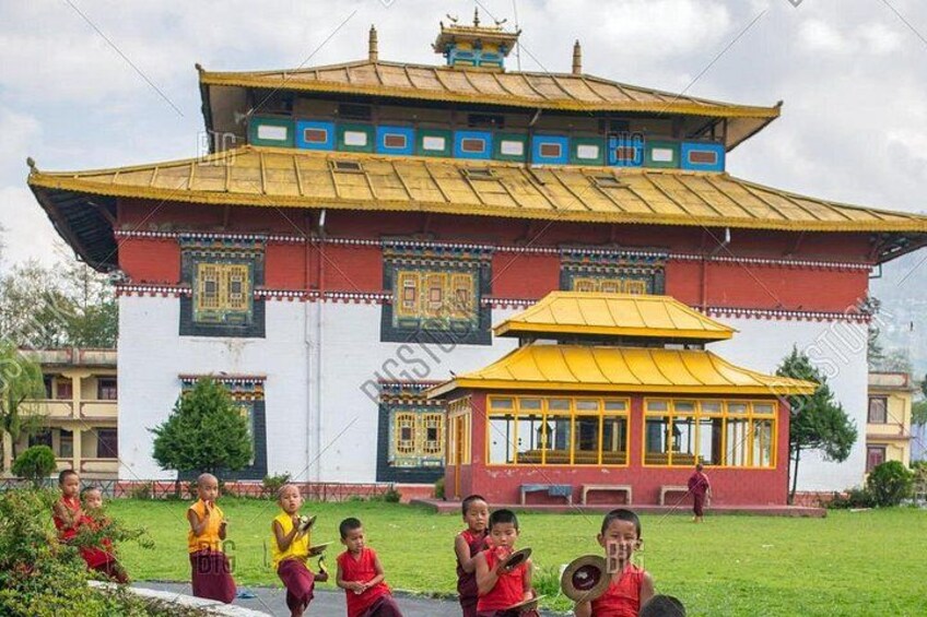 A traditional building with a yellow roof and red walls, surrounded by a grassy area with children playing. 1