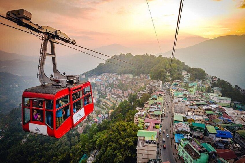 A red cable car moving over a densely populated area with buildings and roads below. 2