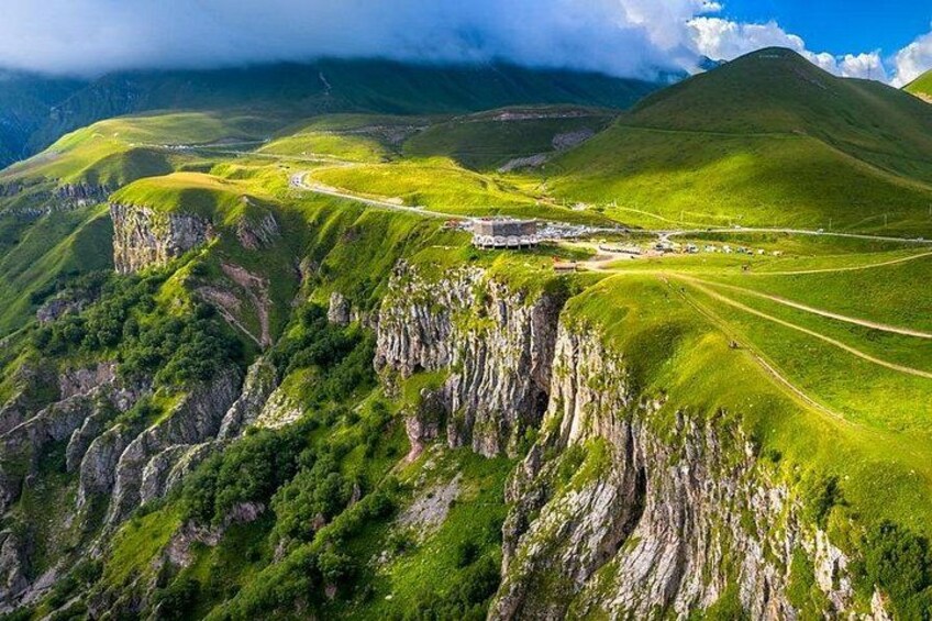 Un paysage montagneux avec une route sinueuse, des champs verdoyants et des falaises rocheuses. 2