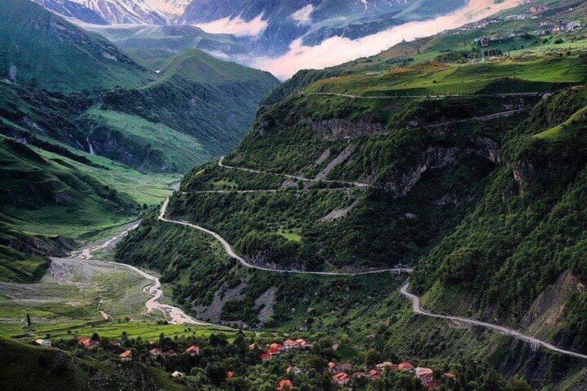 Un paisaje montañoso con una carretera sinuosa, campos en terrazas y un pequeño asentamiento. 3