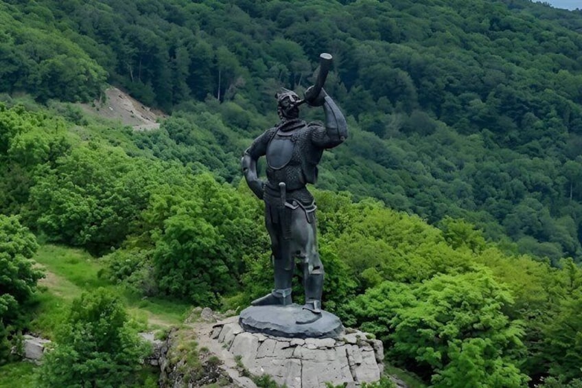A statue of a warrior on a rocky outcrop surrounded by dense forest. 5