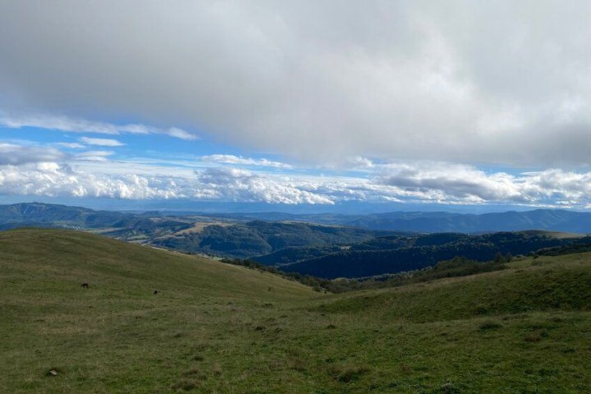 Una colina cubierta de hierba con un valle y montañas lejanas bajo un cielo nublado. 3