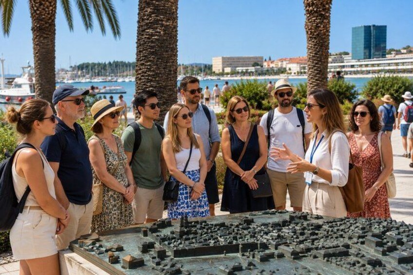 A group of people standing in a sunny outdoor area with palm trees and a body of water in the background. 5