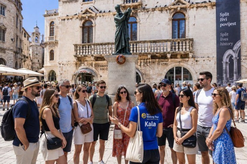 A group of people standing in a square with historical buildings and a statue in the background. 4