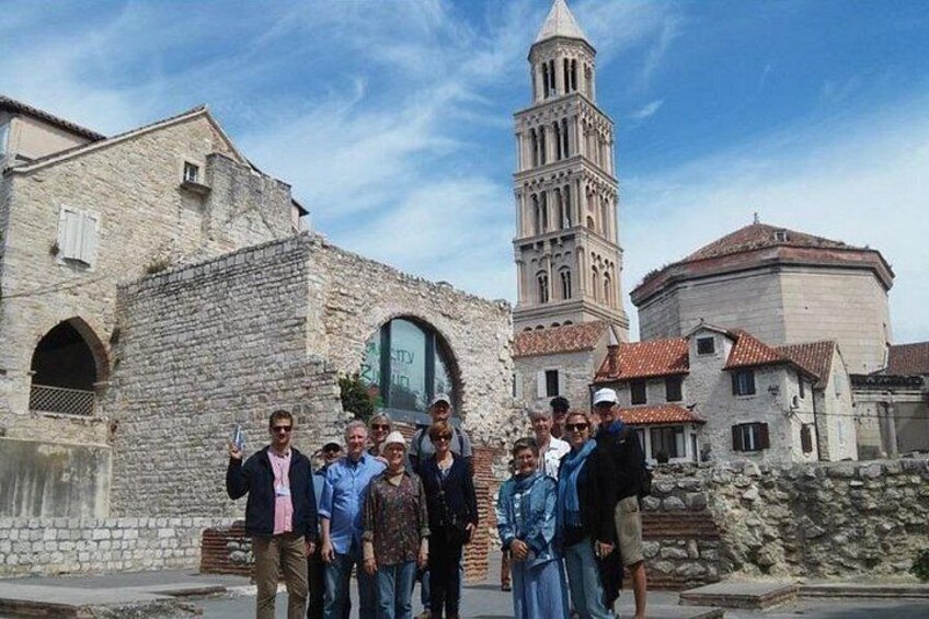 A group of people standing in front of a historic stone building with a bell tower. 2