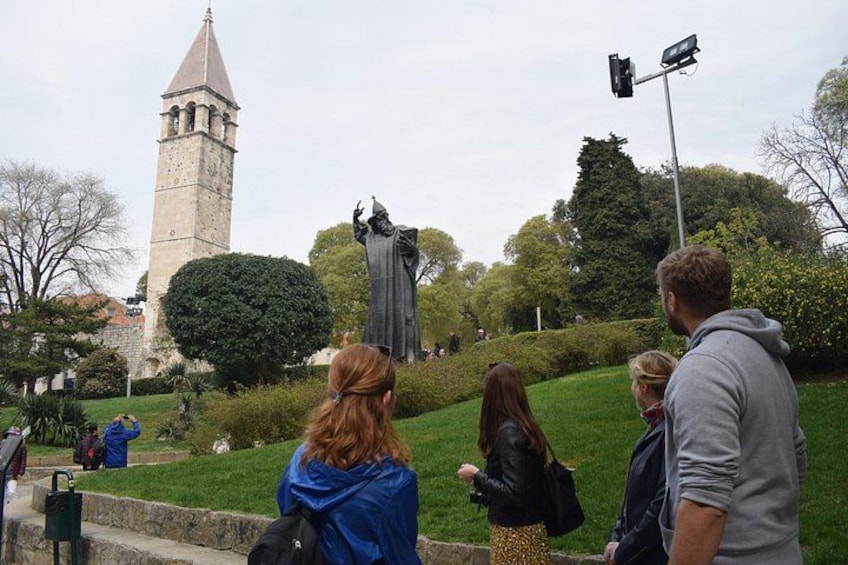 Een standbeeld van een persoon in een park, met een toren op de achtergrond. 3