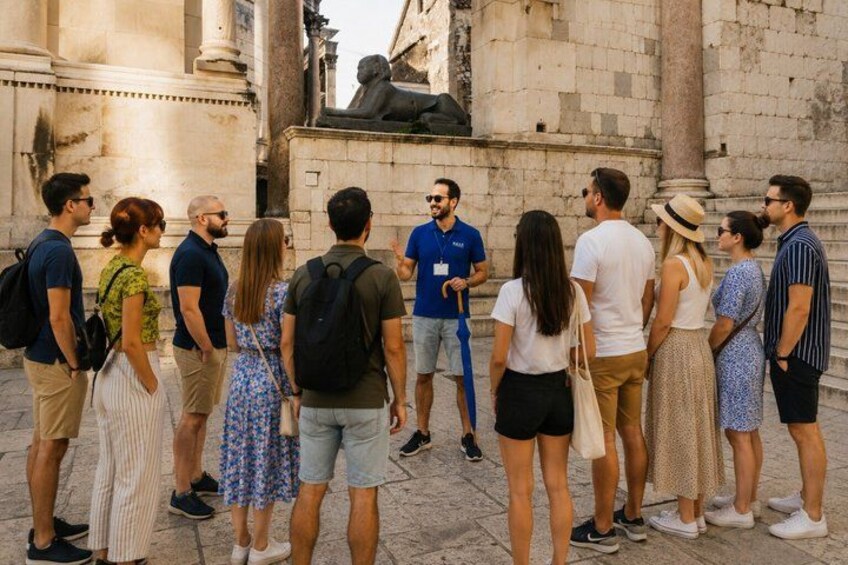Un gruppo di persone in una piazza storica con architettura classica, tra cui colonne e statue. 3