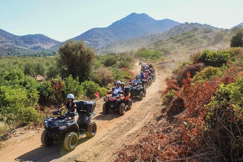 Un grupo de personas en cuatrimotos por un camino de tierra rodeado de vegetación y montañas. 1