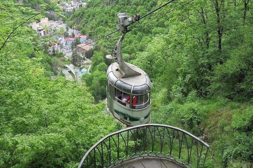 A cable car suspended over a lush green valley with a village below. 5