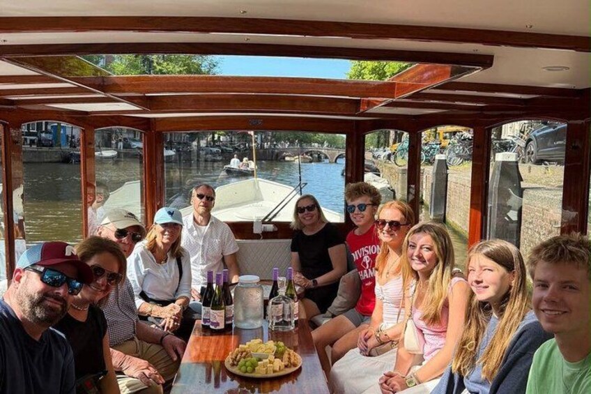 Un groupe de personnes se trouve sur un bateau, autour d’une table dressée pour un repas, et est entouré d’eau et de bâtiments. 4