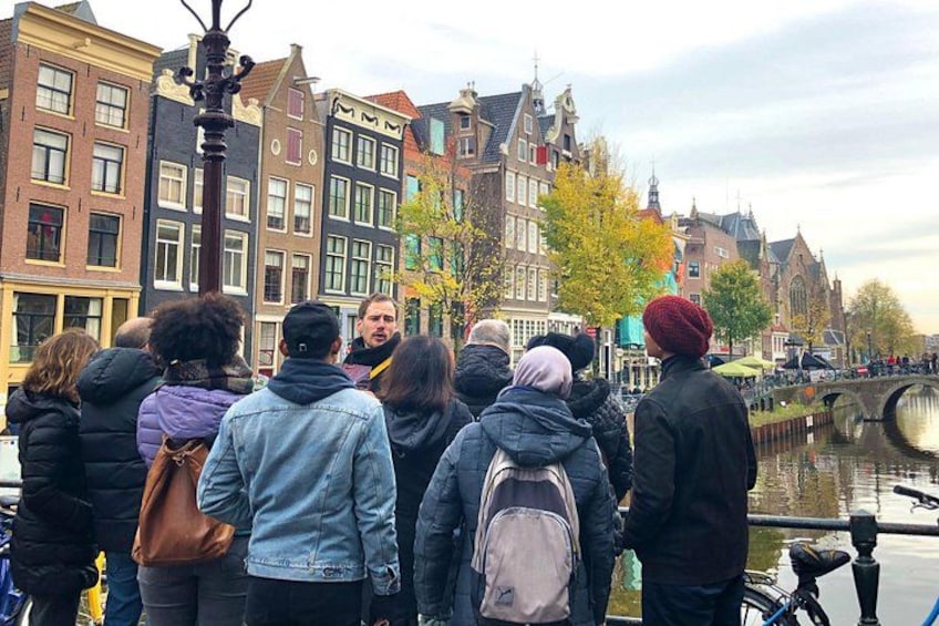 Un groupe de personnes se tient près d’un canal dans une ville historique, avec des bâtiments et un pont en arrière-plan. 4