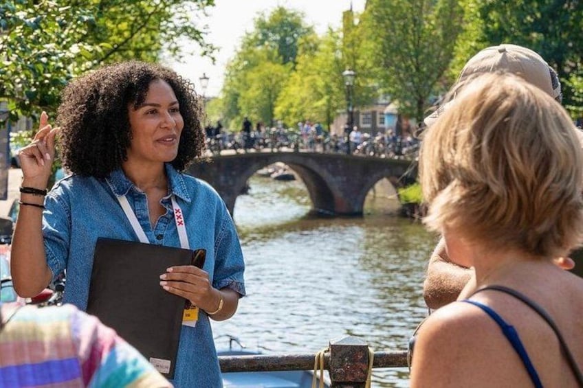 Une personne vêtue d’une chemise bleue, tenant un classeur, se tient au bord d’une rivière, avec un pont en arrière-plan. 3