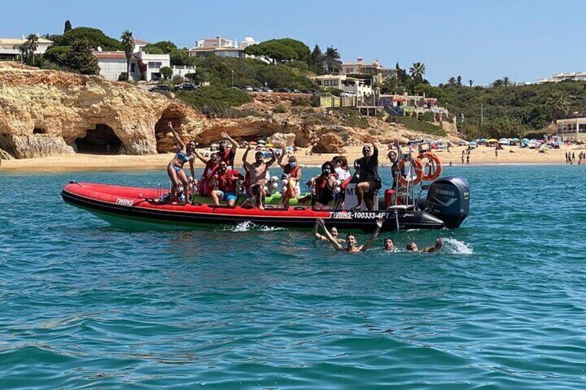 Un bateau rouge avec des personnes à bord, de l’eau et une plage avec des bâtiments en arrière-plan. 3