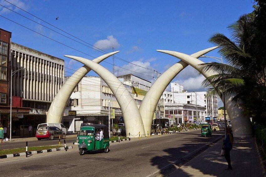 Una calle con un arco blanco característico, un auto-rickshaw verde y un peatón. 2