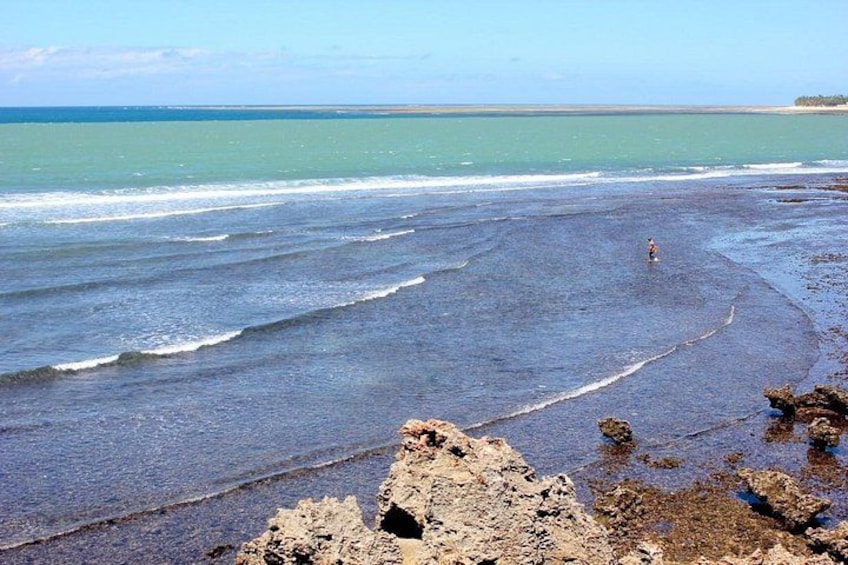 Una playa con olas, una persona y afloramientos rocosos. 4