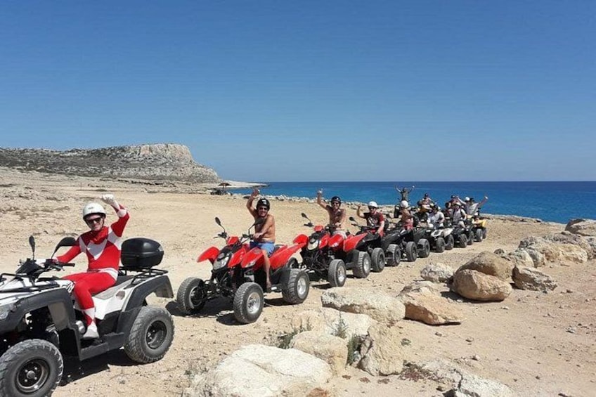 Een groep mensen op rode terreinwagens op een rotsachtig strand, met de zee op de achtergrond. 1