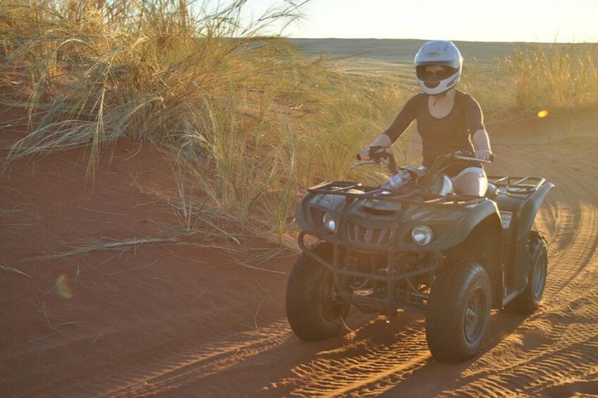 Iemand rijdt op een quad over een zandpad, omringd door droog gras en rode aarde. 3