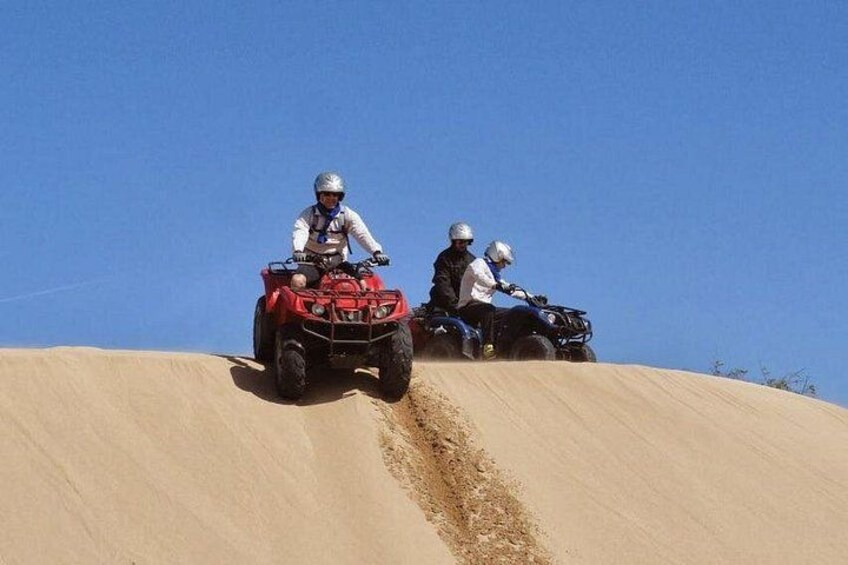 Twee personen rijden op quadbikes over een zandige helling onder een heldere lucht. 5