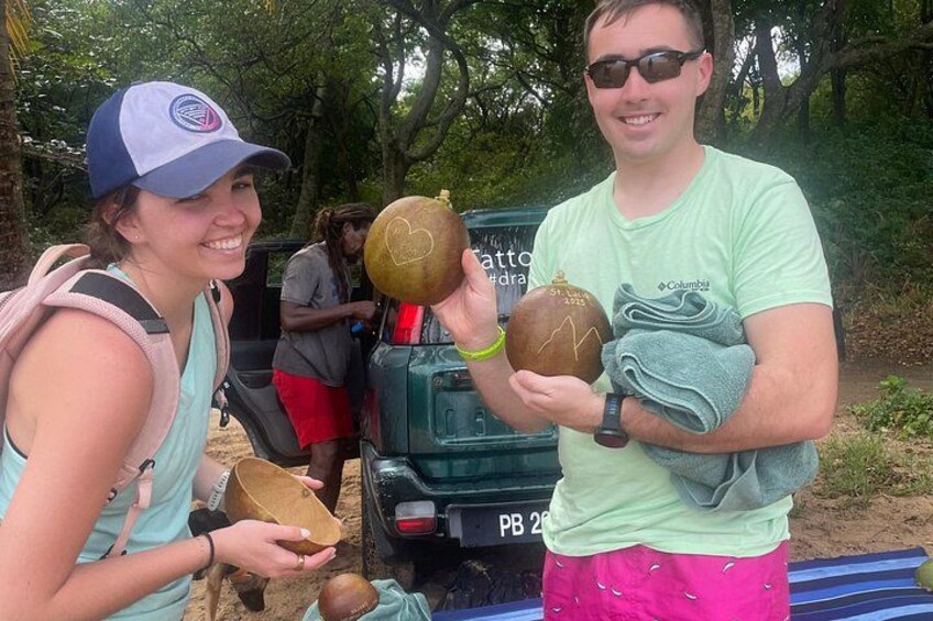 Two people holding large gourds, a vehicle, and a forested area. 1
