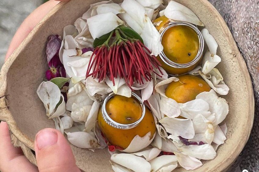 A bowl with three small containers, surrounded by white flower petals and a red flower. 2