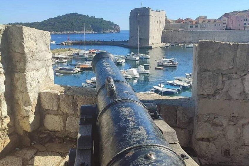 A cannon overlooking a harbor with boats and a castle in the background. 3