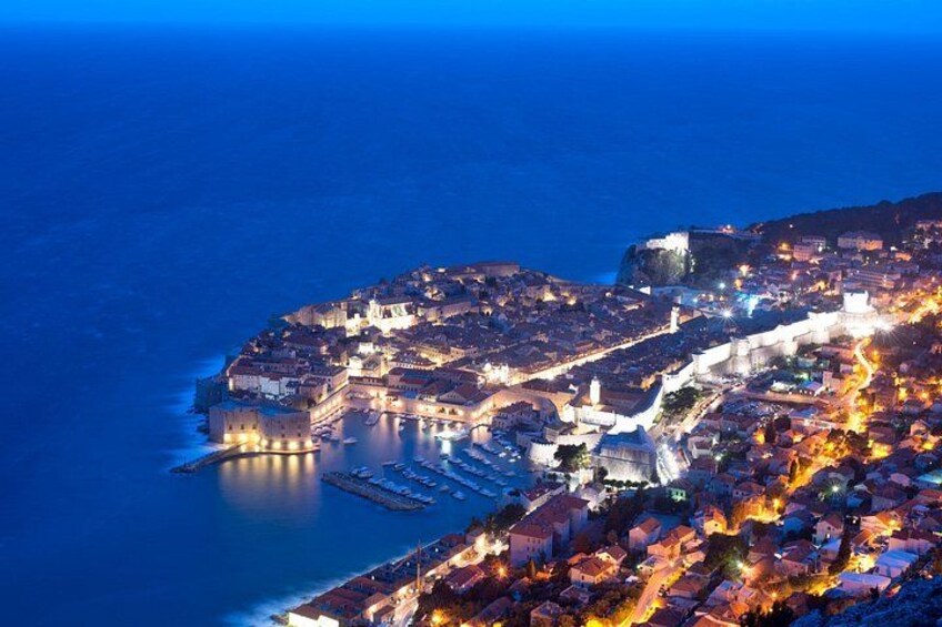 A coastal town at night with illuminated buildings and a prominent castle on a hill. 4