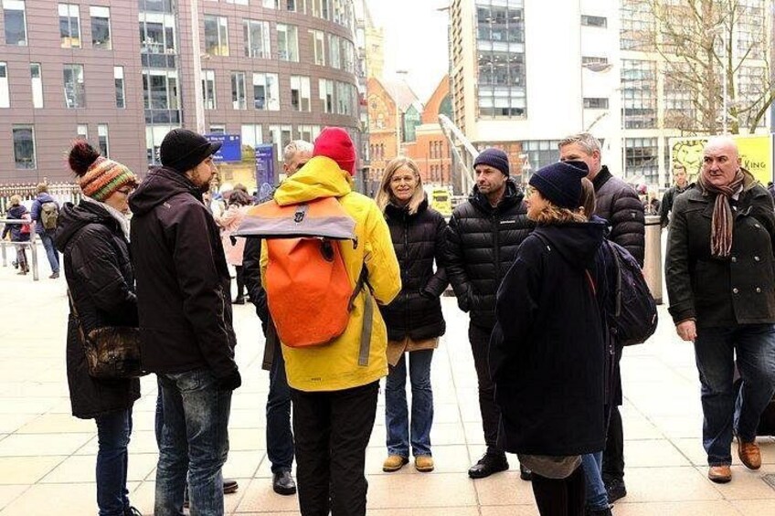 A group of people standing on a sidewalk in an urban area with buildings in the background. 2