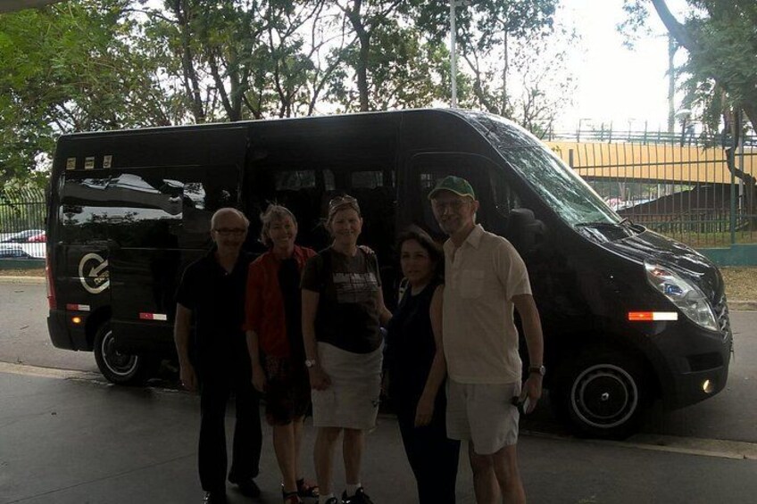 A group of people standing in front of a black van. 1
