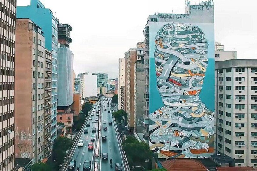 A cityscape with a large mural on a building, a busy highway, and surrounding high-rise buildings. 5