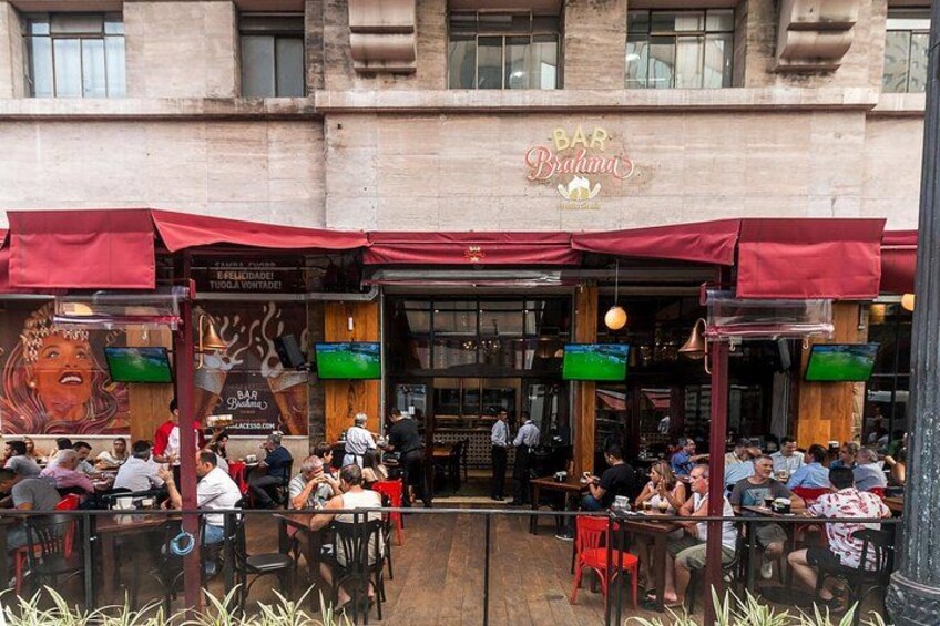 An outdoor cafe with red awnings, outdoor seating, and a mural on the building. 3