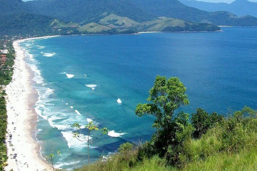 A coastal landscape with a sandy beach, clear blue waters, and green hills in the background. 3