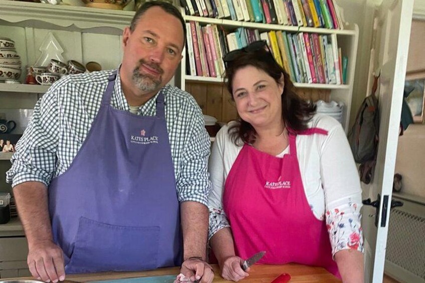 Two people wearing aprons with the text 'KATES BY PLACE' standing in a kitchen with a bookshelf in the background. 5