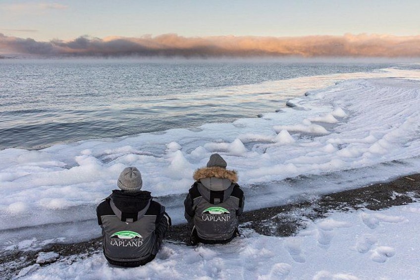Dos personas sentadas en una playa nevada, con un mar congelado al fondo. 2