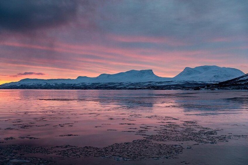 Un lago congelado con montañas al fondo y un cielo rosado. 4