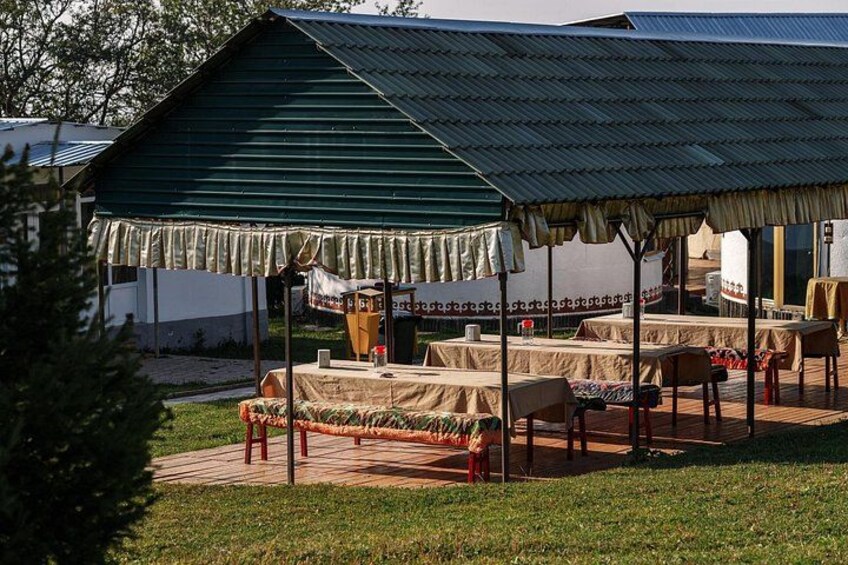 A rustic outdoor dining area with tables and chairs under a green-roofed pavilion. 4