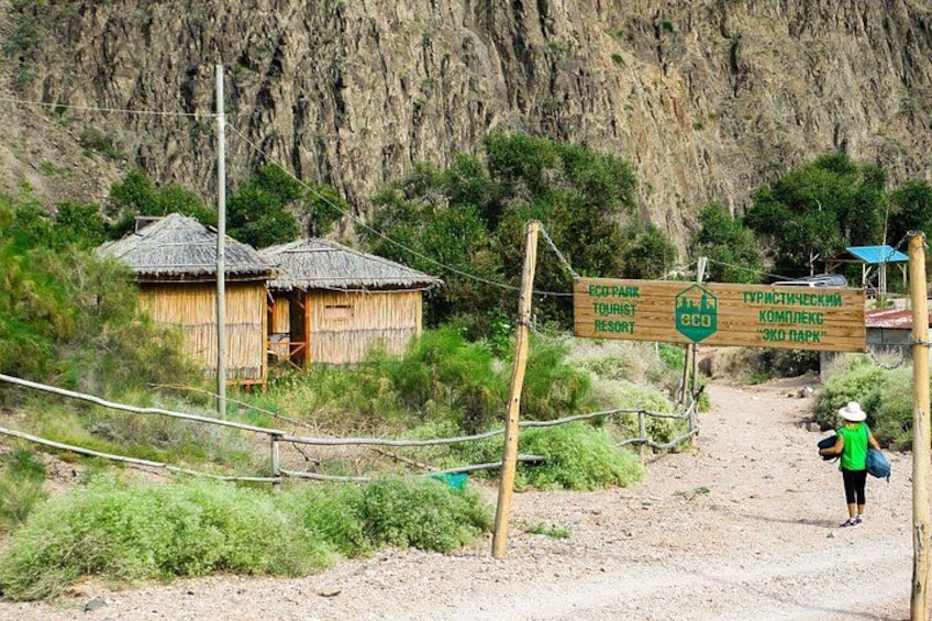 Ein Feldweg führt zu einem Berg mit einem Schild und strohgedeckten Hütten. 3