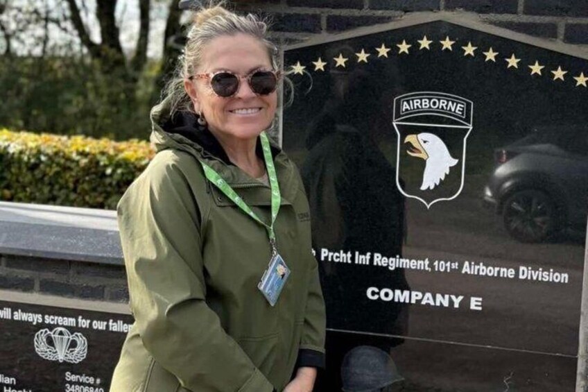 Una persona in piedi di fronte a una targa commemorativa con l'iscrizione 'Prakt Inf Regiment, 101st Airborne Division COMPANY E' e un emblema con un'aquila. 1