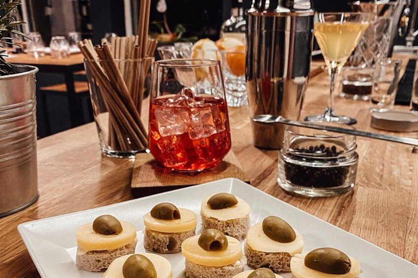 Eine Dessertplatte mit kleinen Kuchen, die mit Oliven belegt sind, ein Glas roter Saft und ein Cocktail-Shaker auf einem Holztisch. 4