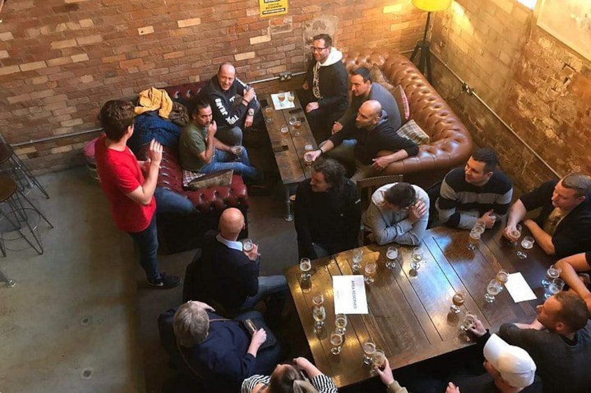A group of people seated around a wooden table in a brick-walled room with a leather couch. 4
