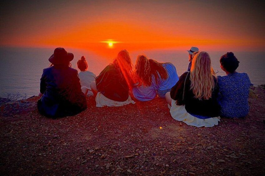 Een zonsondergang boven de oceaan, met mensen zittend op een rotsachtige kust. 3