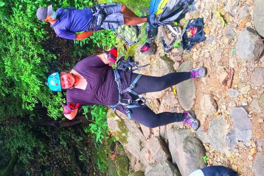 Una persona con una maglietta viola e pantaloni neri, con un casco, in piedi su un sentiero roccioso con zaini. 3