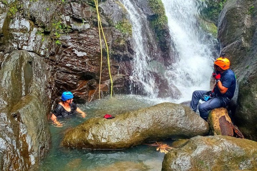 Due persone con caschi e giubbotti di salvataggio vicino a una cascata in un'area rocciosa. 2