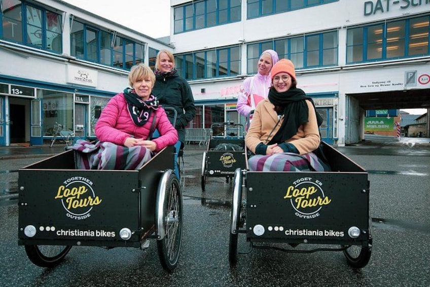Två personer i rullstol med en skylt där det står ”Guidade turer” och ”Christiania-cyklar”. 2