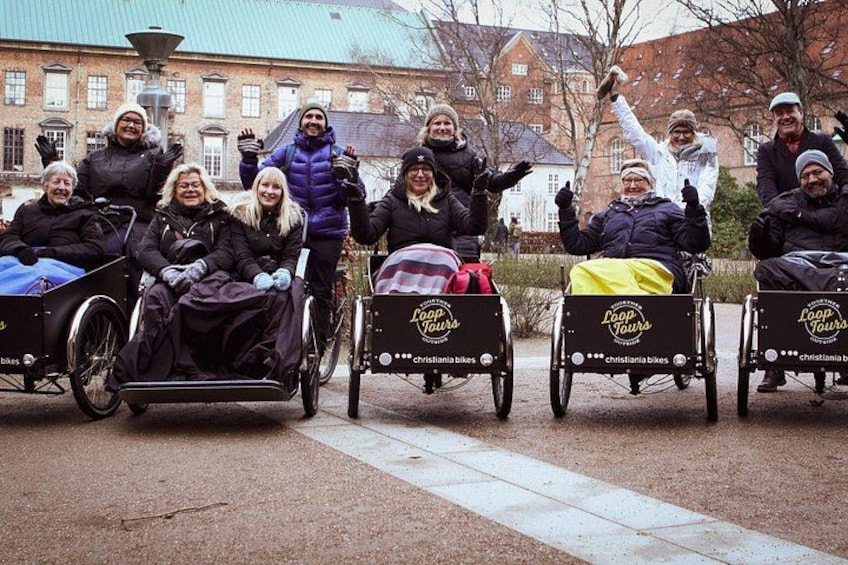 Personer i rullstolar med skyltar som visar att de deltar i en "Loop Tour", en byggnad och ett asfalterat område. 4